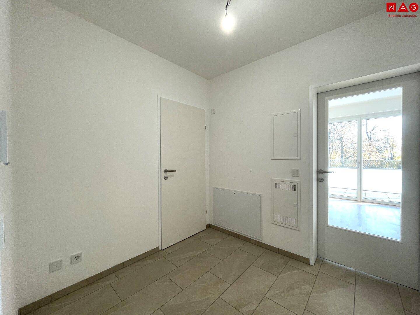 Heller Eingangsbereich mit Fliesenboden und Zugang zu einem Außenbereich.