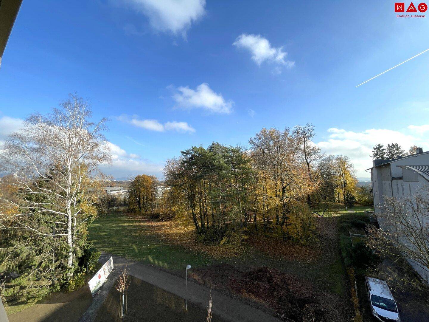 Weitläufiger Blick ins Grüne mit herbstlichen Bäumen und einem klaren Himmel.