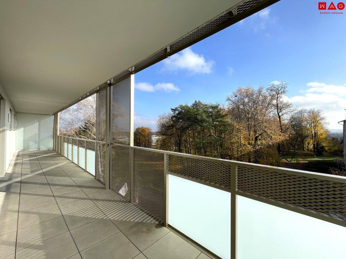 Langer, sonniger Balkon mit Fliesenboden und weitem Blick ins Grüne.