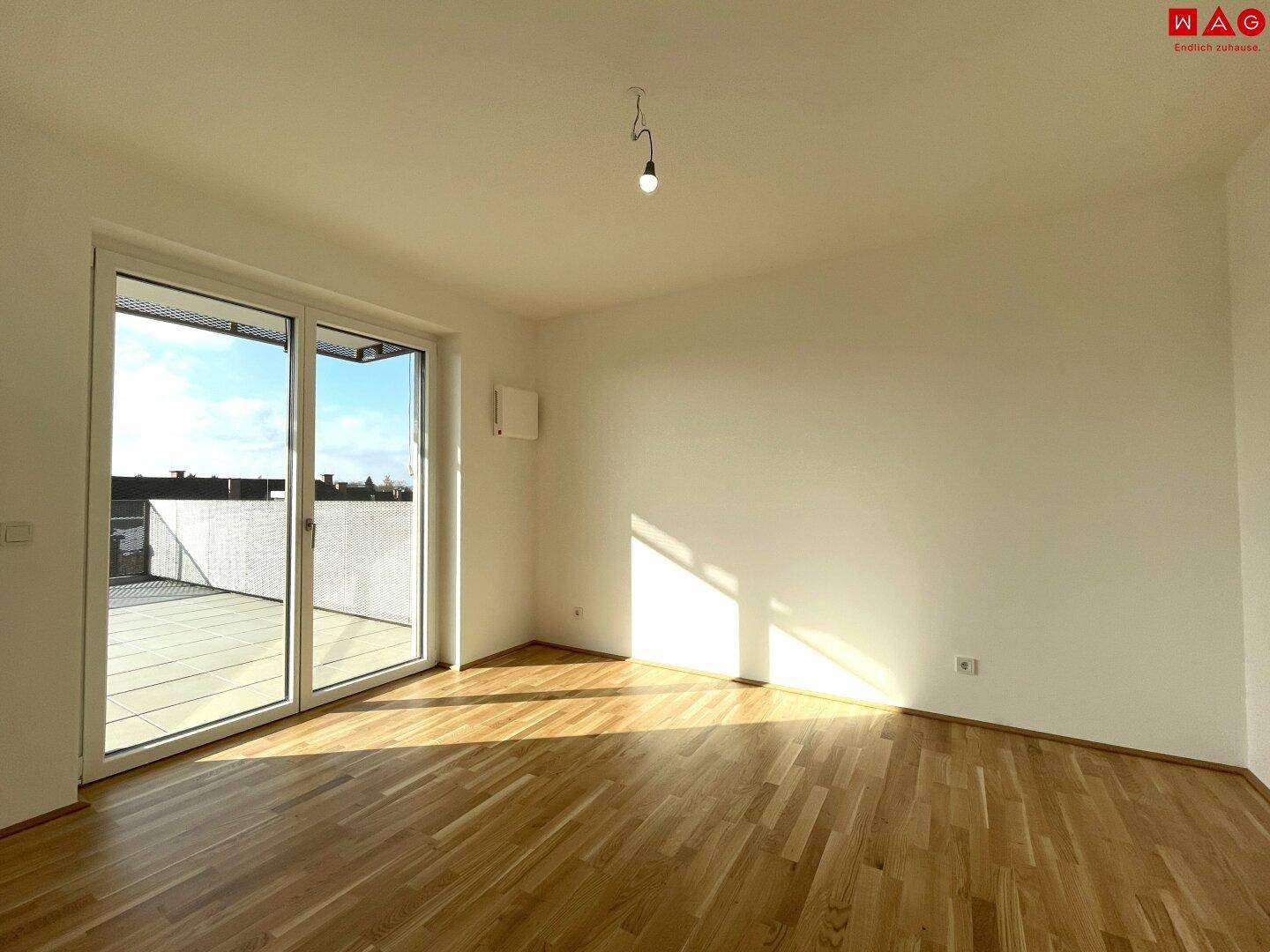 Unmöbliertes Schlafzimmer mit Holzboden und großen Fenstern, die viel Sonnenlicht hereinlassen.
