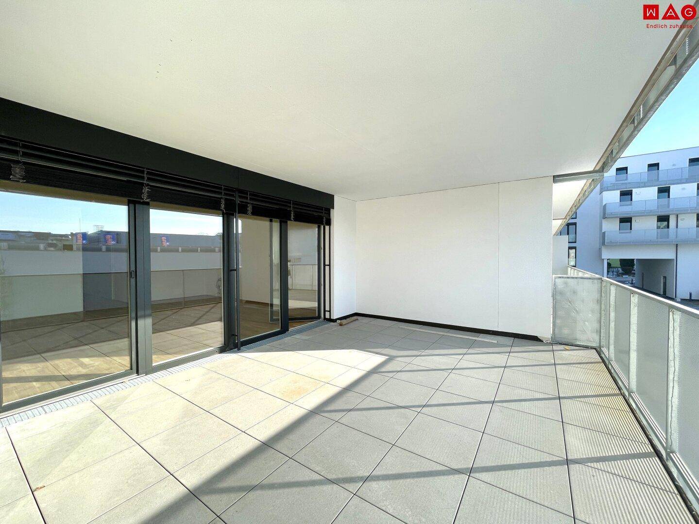 Geräumiger, leerer Balkon mit Fliesenboden und Glasgeländer, ideal für Entspannung im Freien.