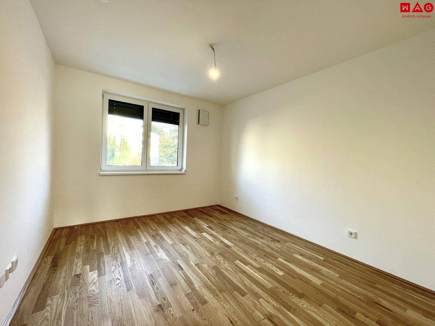 Leeres Schlafzimmer mit Holzboden und Fenster, bereit für individuelle Gestaltung.