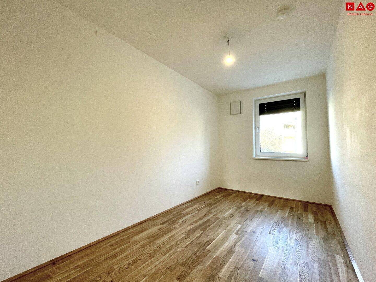 Leeres Zimmer mit Holzboden und Fenster, ideal als Kinder- oder Arbeitszimmer.