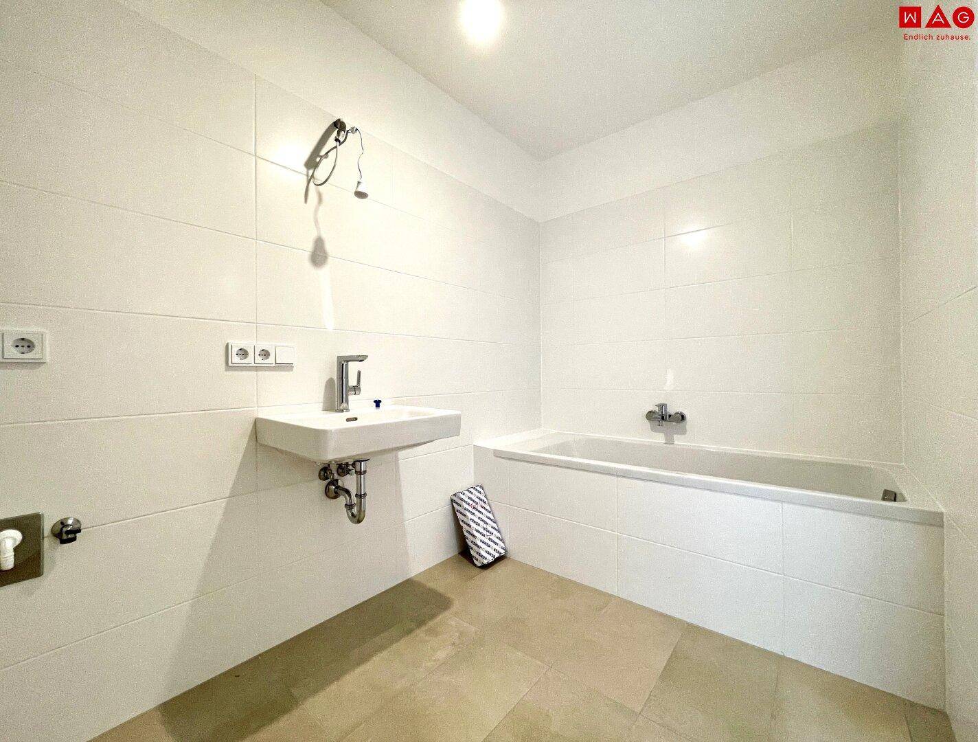 Helles Badezimmer mit Badewanne und Waschbecken, gefliest und bereit zur Einrichtung.