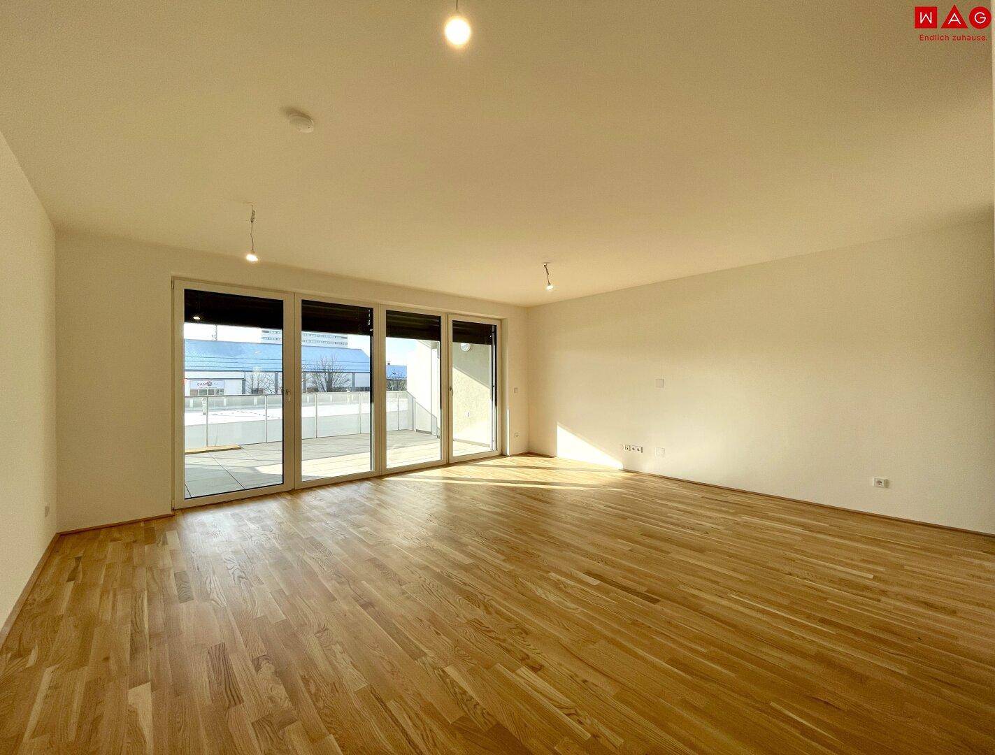 Geräumiges, leeres Wohn-Esszimmer mit Holzboden und großen Fenstern zur Terrasse.