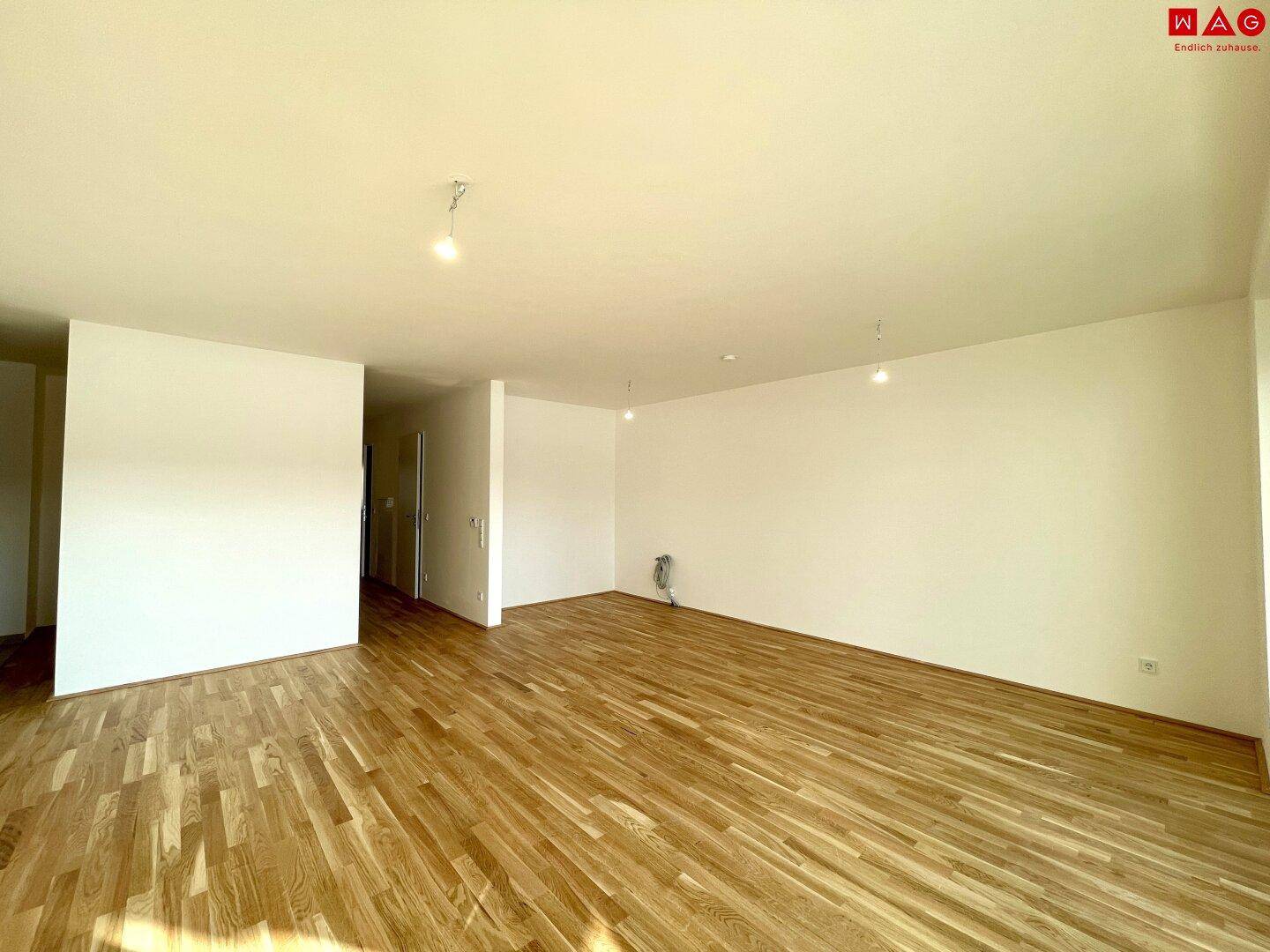 Heller, leerer Wohnbereich mit Holzboden und weiß gestrichenen Wänden, bereit zur Einrichtung.