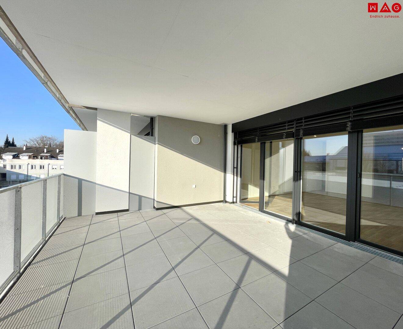 Geräumige, geflieste Terrasse mit viel Sonnenlicht und Blick auf die umliegenden Gebäude.