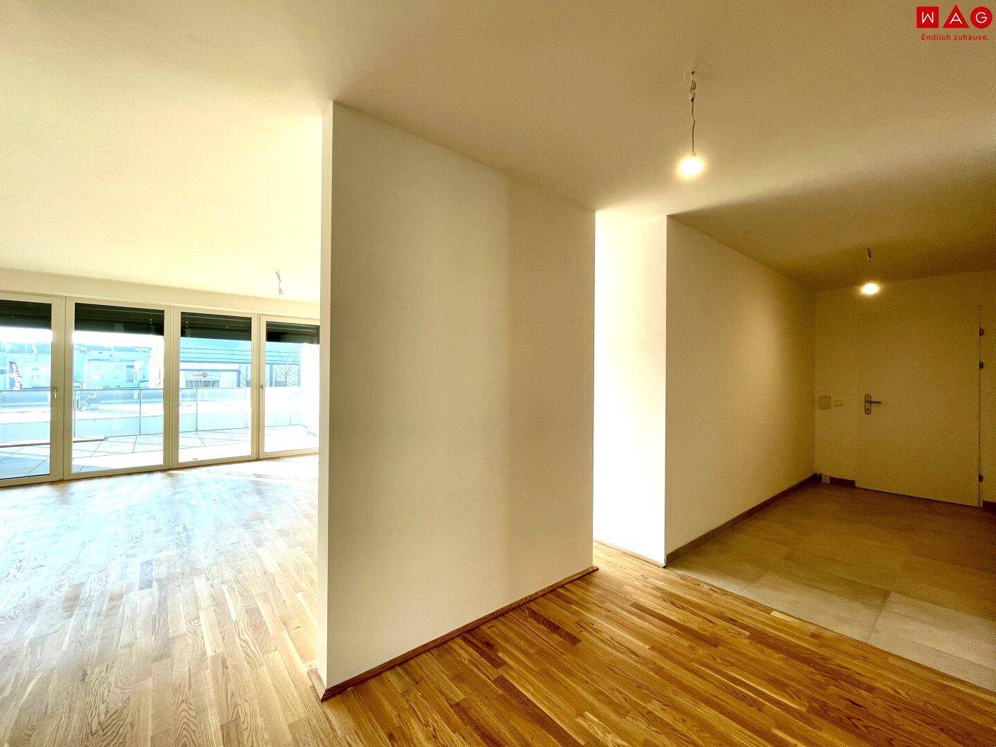 Übergangsbereich vom Flur zum Wohnzimmer mit Holzboden und viel Tageslicht.