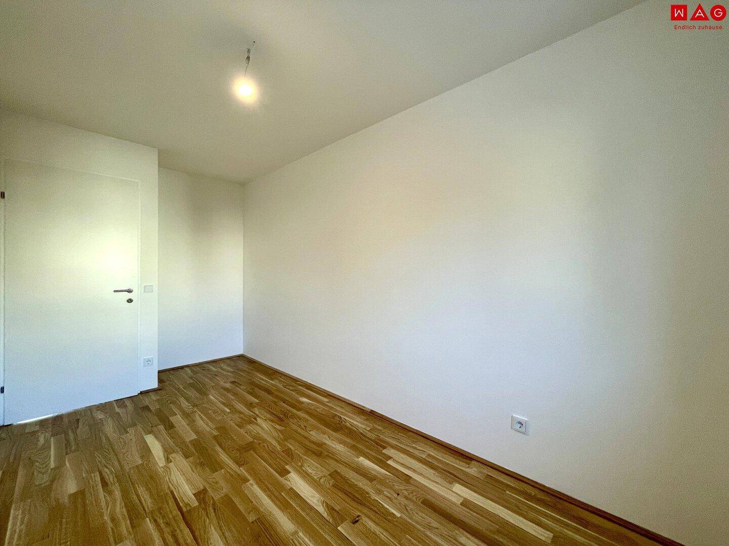 Helles, leeres Schlafzimmer mit Holzboden und weiß gestrichenen Wänden.