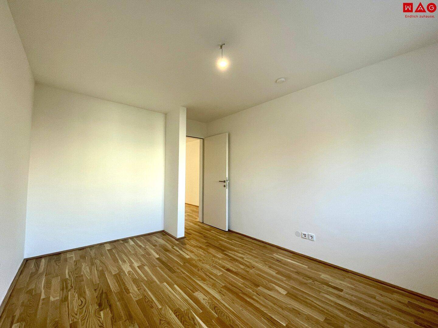 Helles, leeres Zimmer mit Holzboden und weiß gestrichenen Wänden, vielseitig nutzbar.