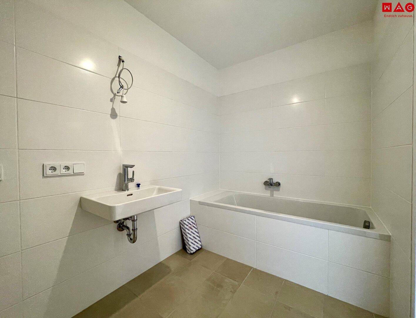 Helles Badezimmer mit Badewanne und Waschtisch, komplett gefliest in neutralen Farben.