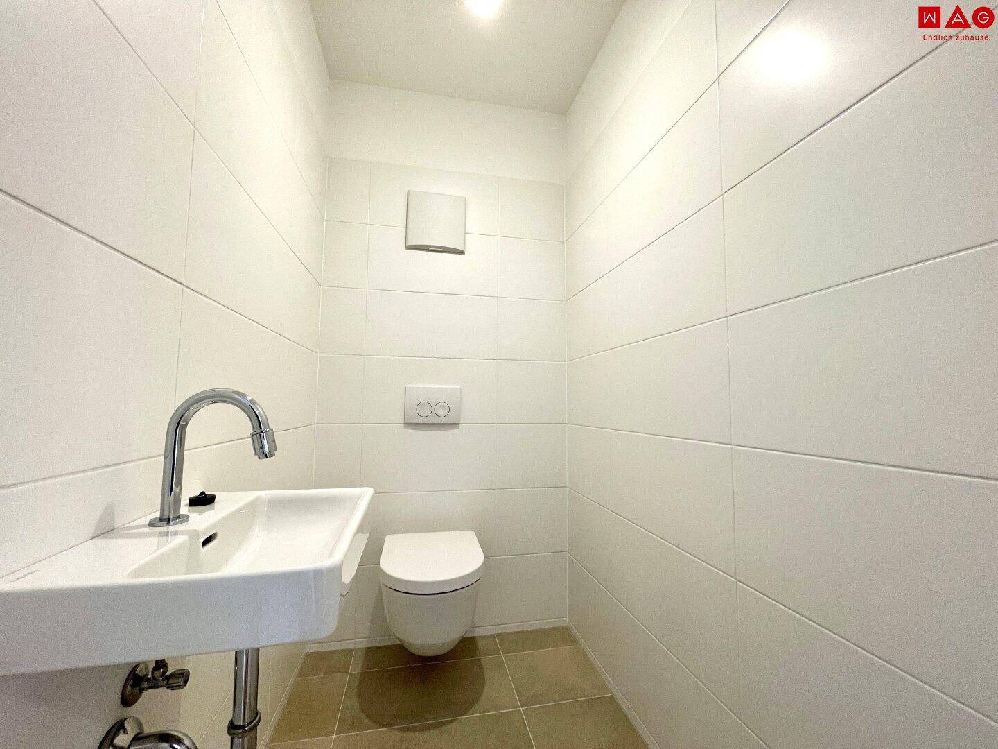 Helles, gefliestes Gäste-WC mit wandhängender Toilette und kleinem Waschtisch.