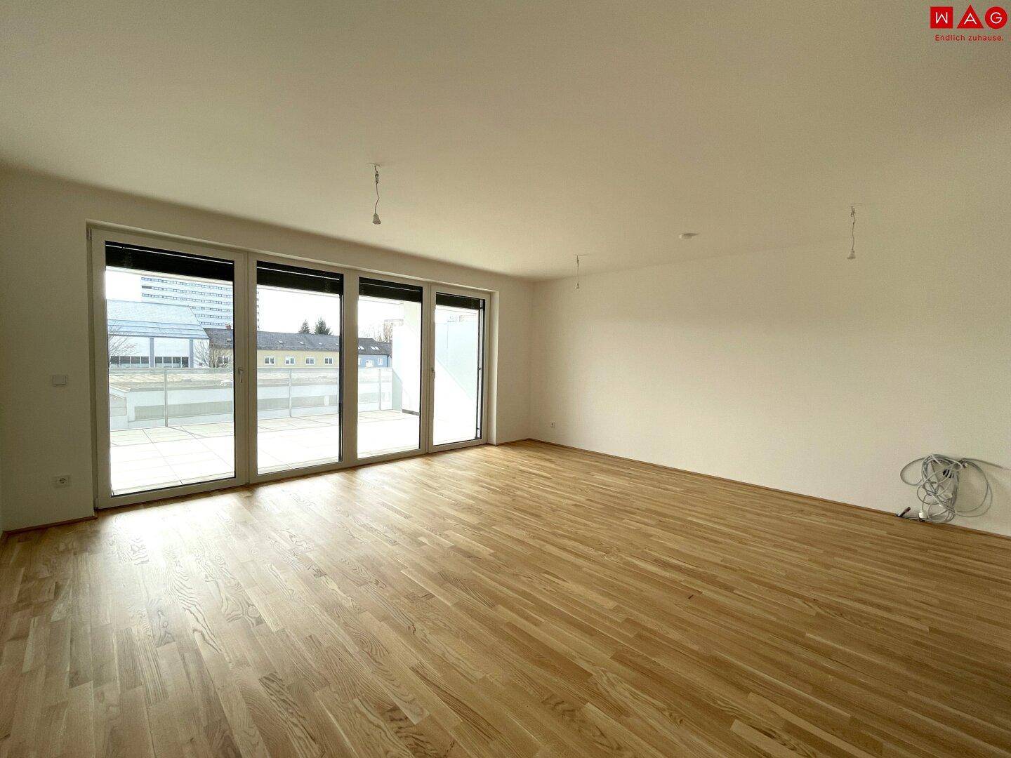 Heller, leerer Raum mit großen Fenstern und Holzboden, bereit zur individuellen Gestaltung.