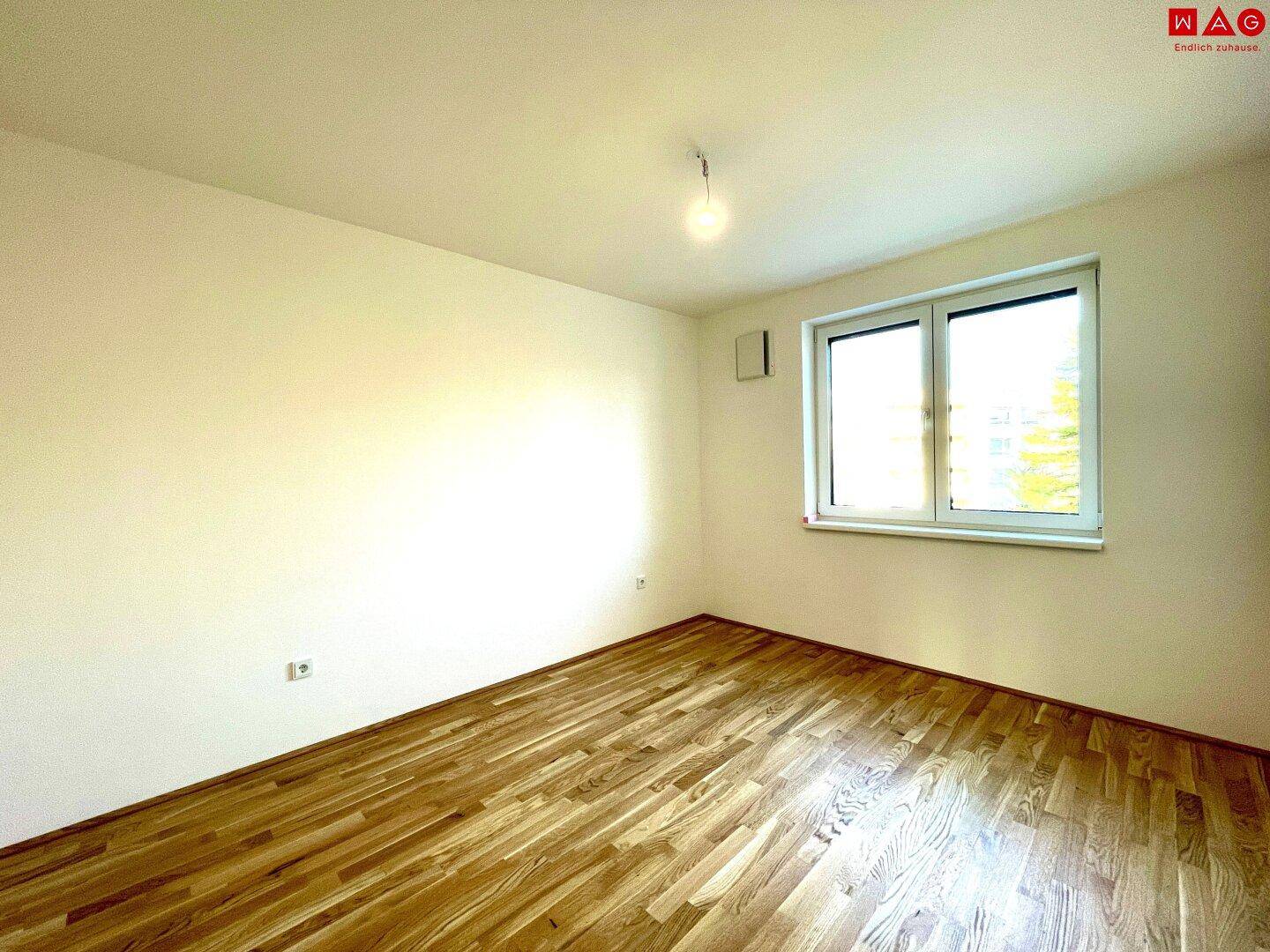 Helles, leeres Schlafzimmer mit Holzboden und Fenster, ideal für individuelle Gestaltung.