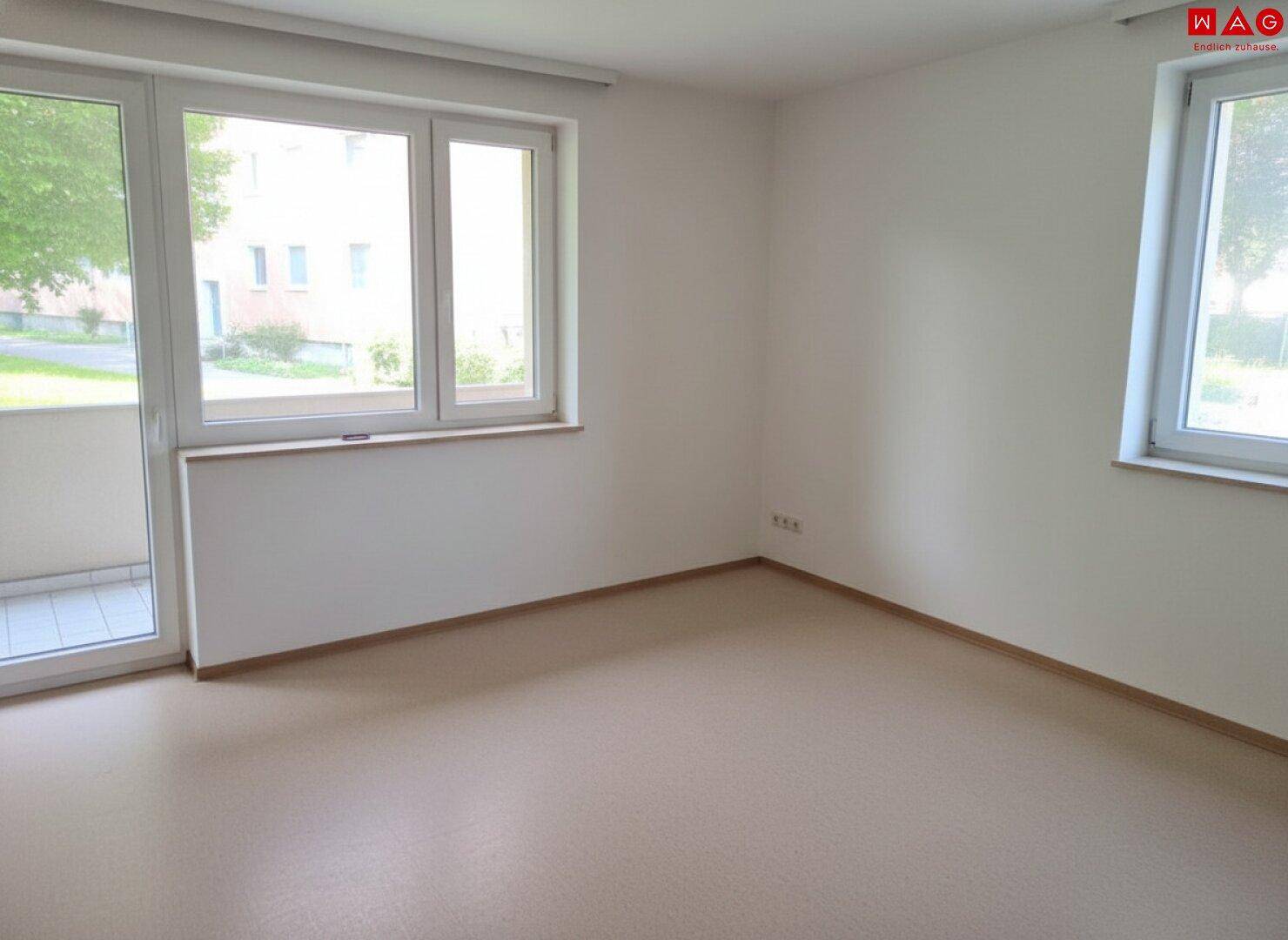 Leerer Raum mit weißen Wänden, Vinylboden und großem Fenster mit Balkonzugang.