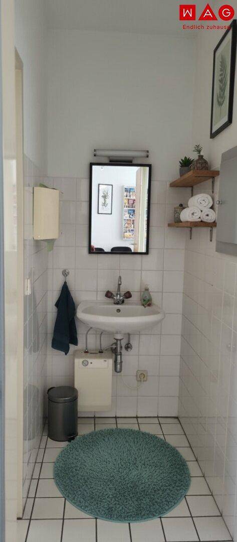 Funktionales Badezimmer mit weißen Fliesen, Waschbecken, Spiegel und einem kleinen Mülleimer.