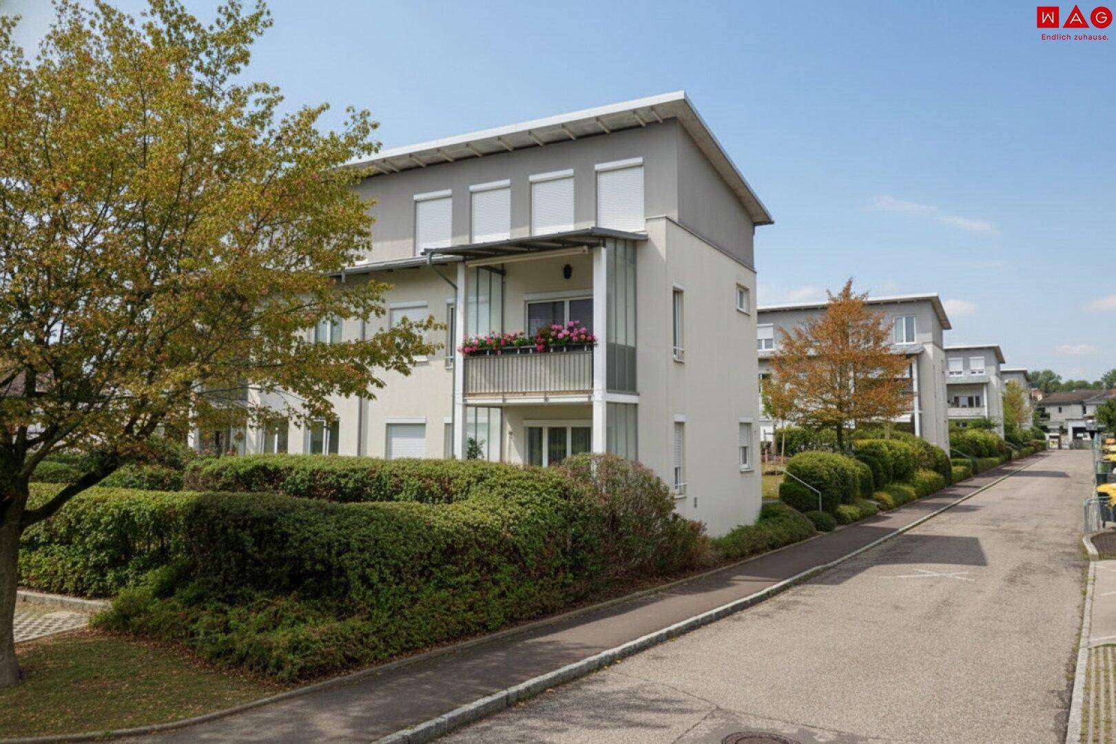 Mehrfamilienhaus mit modernen Balkonen und gepflegter Grünanlage entlang einer ruhigen Wohnstraße.