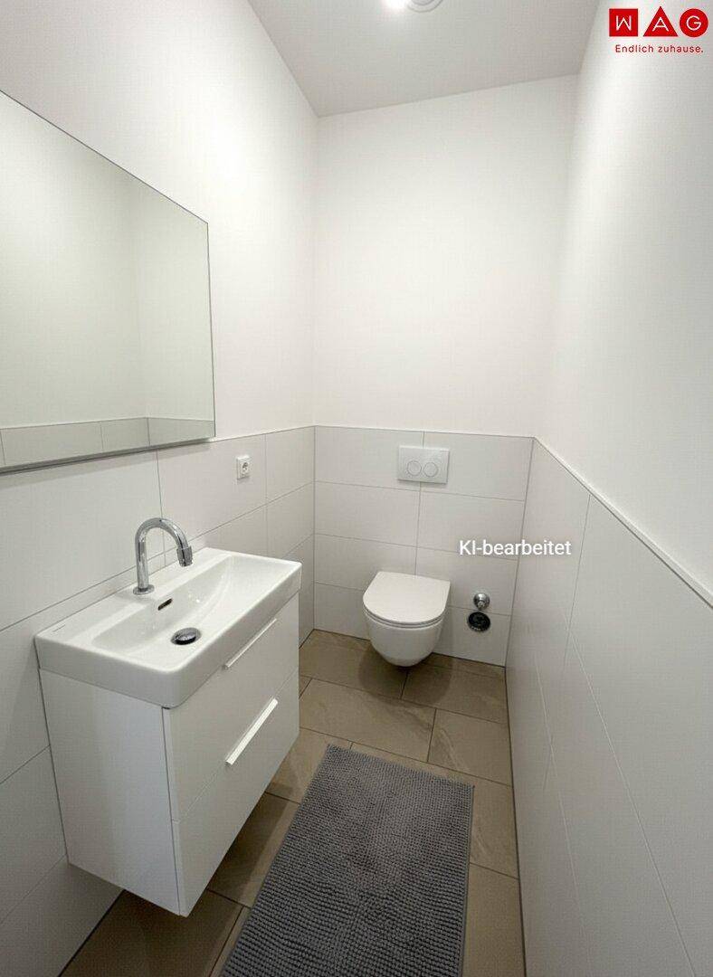 Funktionales Gäste-WC mit wandhängender Toilette, Waschbecken und hellen Fliesen.