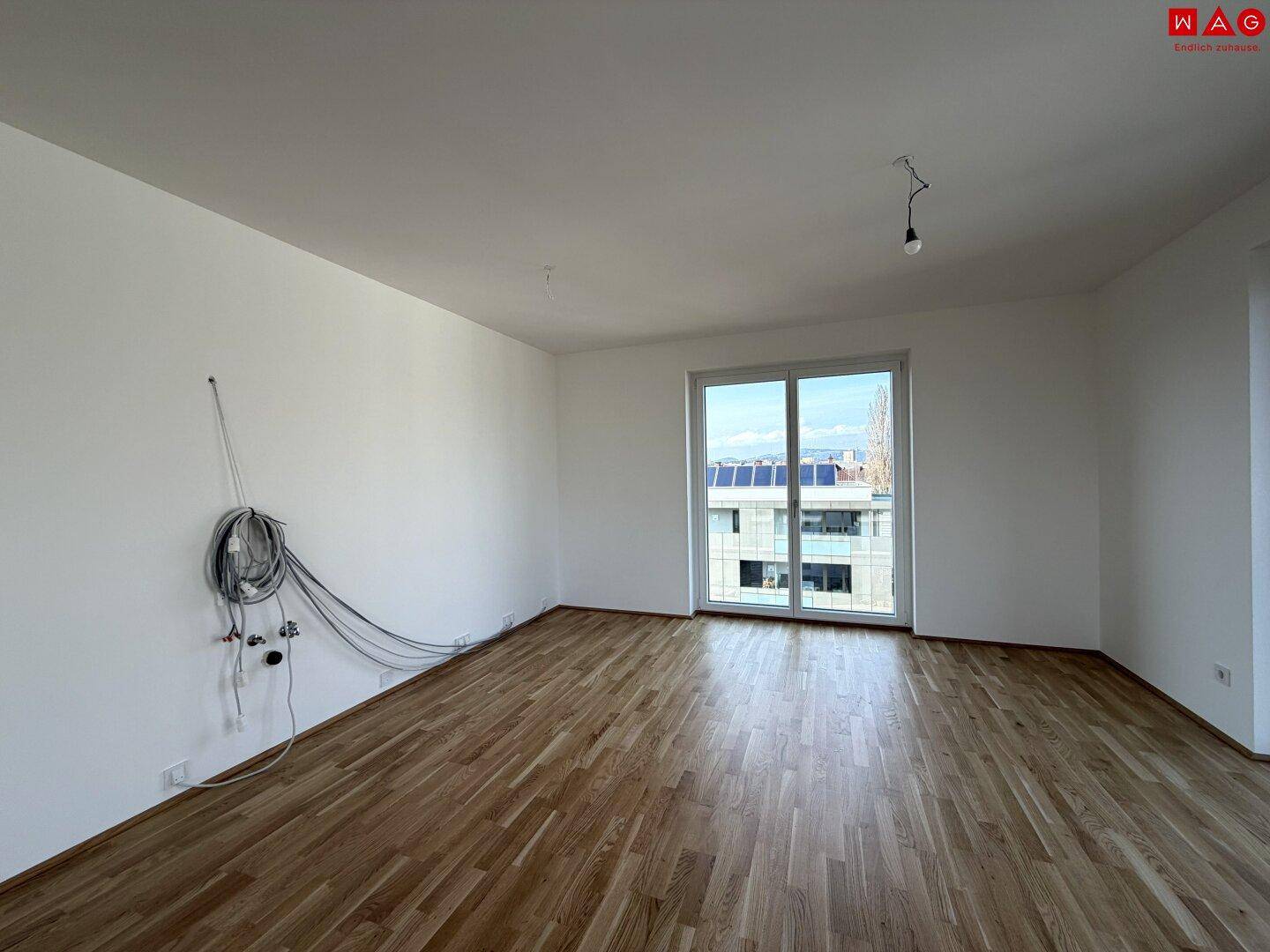 Geräumiges Wohnzimmer mit Holzboden und großen Fenstern, bereit für individuelle Einrichtung.