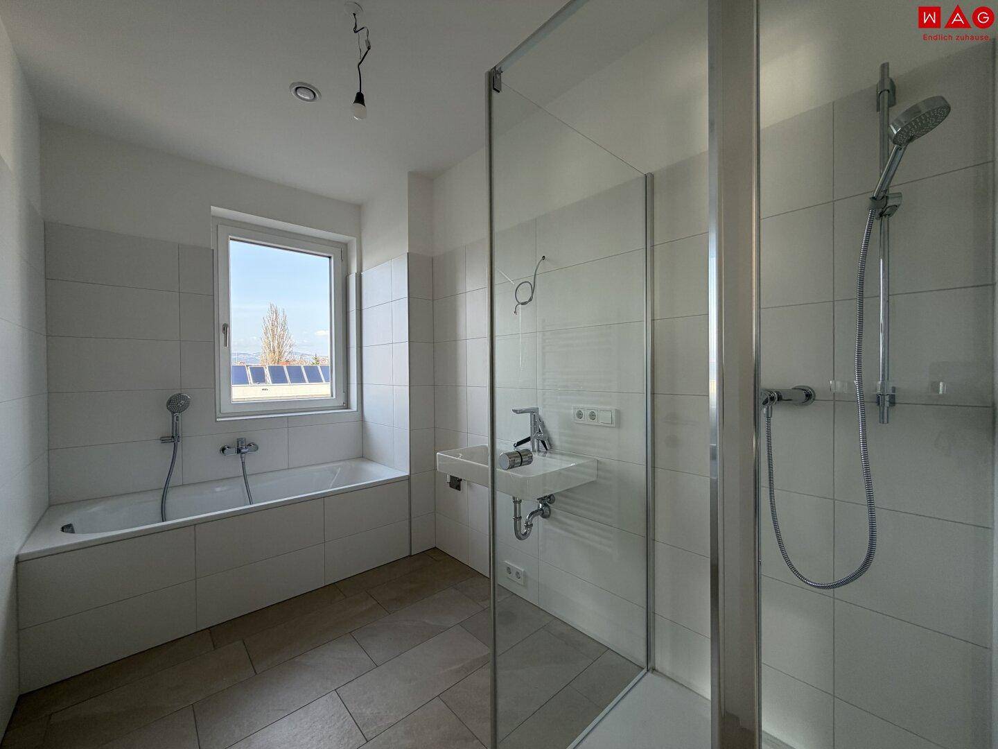 Helles Badezimmer mit Badewanne, Duschkabine und Fenster, bereit für die Endmontage.