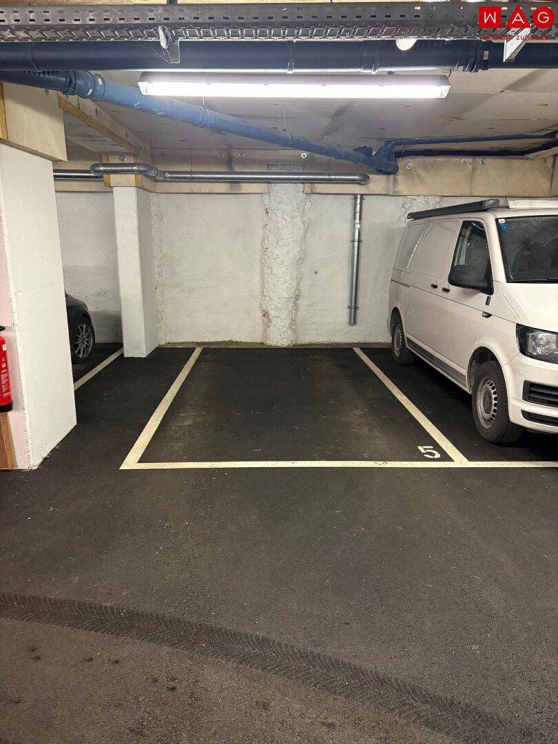 Tiefgaragenstellplatz mit Betonwänden und sichtbaren Leitungen, ein Fahrzeug ist teilweise geparkt.