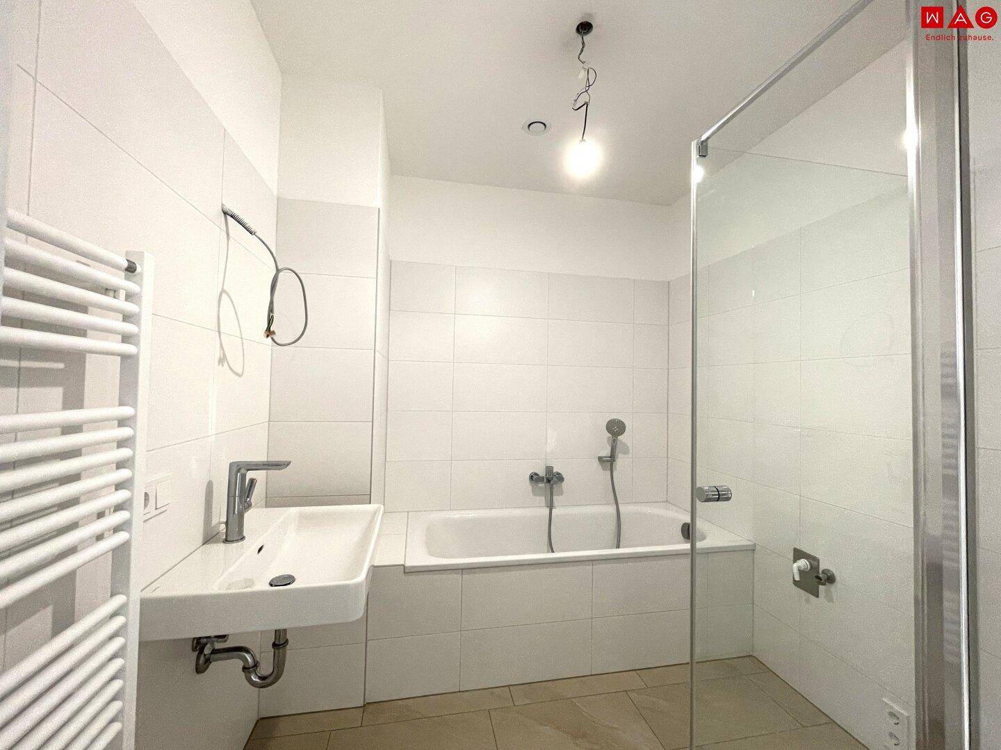 Helles Badezimmer mit Badewanne, Dusche, Waschtisch und praktischem Handtuchheizkörper.