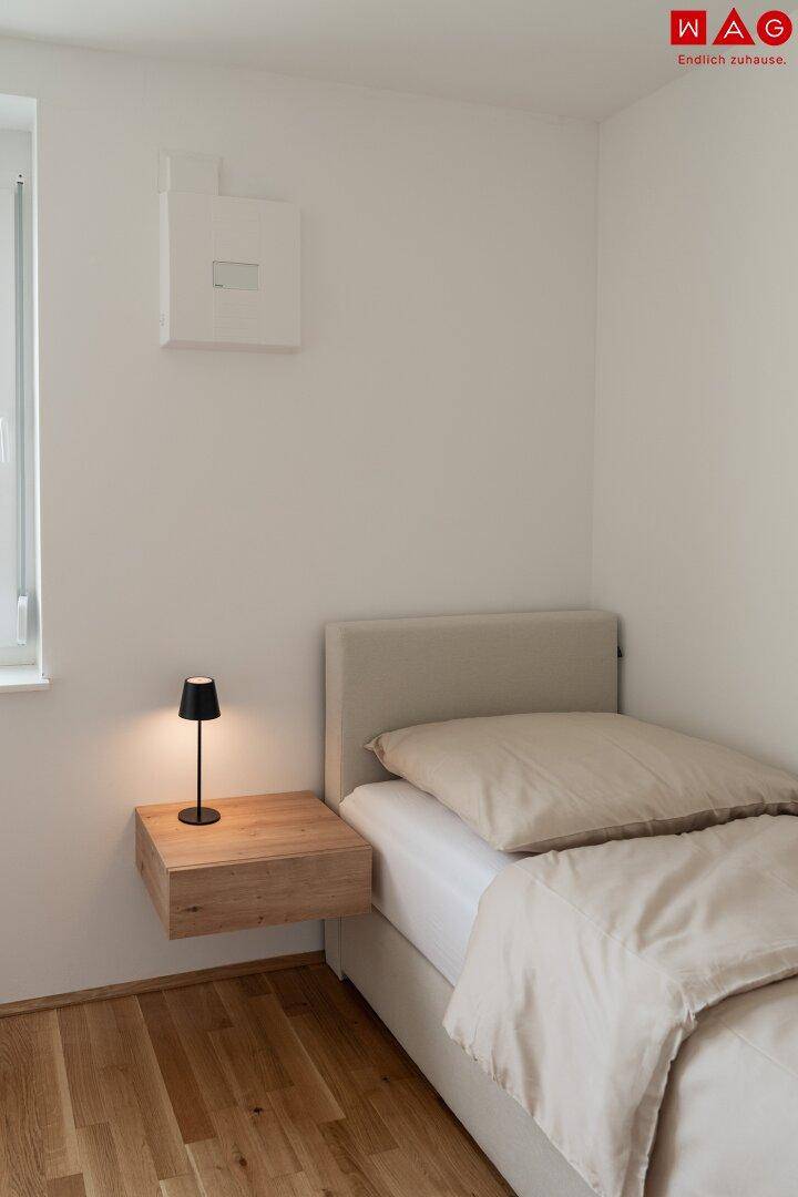 Helles Einzelzimmer mit Bett, schwebendem Nachttisch und Holzboden, ideal als Kinder- oder Gästezimmer.