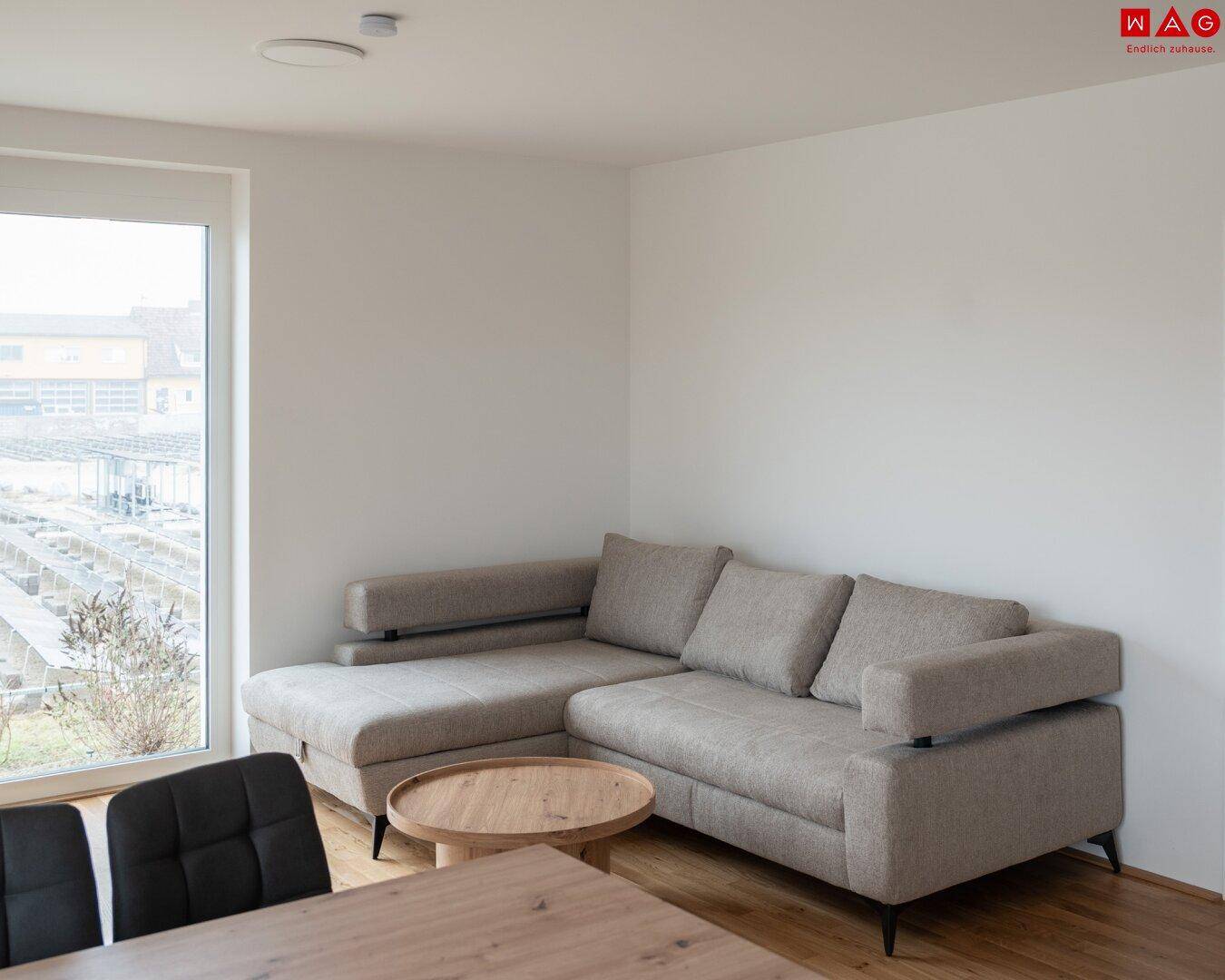 Heller Wohnbereich mit großem Ecksofa, Holzboden und Blick nach draußen, offen zum Essbereich.