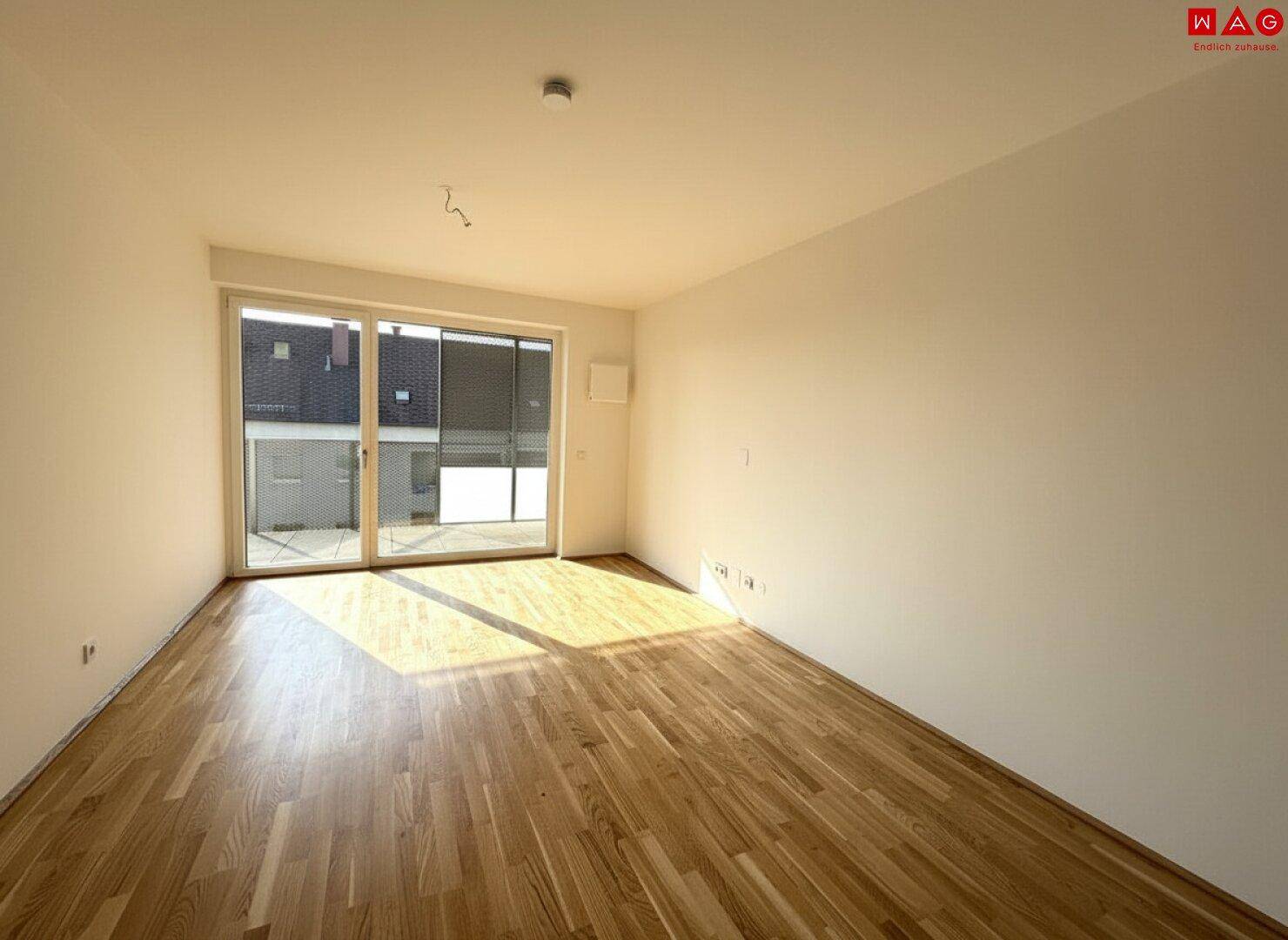 Geräumiger, heller Raum mit Parkettboden und großen Fenstern zum Balkon.