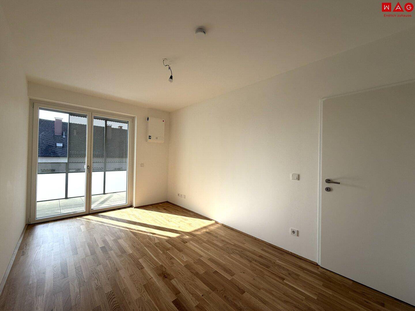 Heller Raum mit Parkettboden und großen Schiebetüren, die auf den Balkon führen.