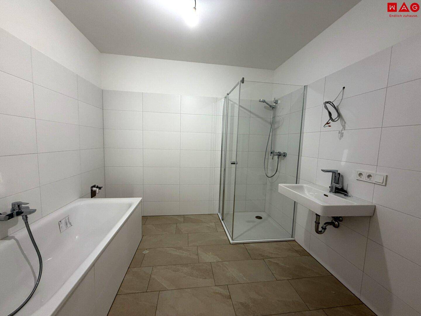 Helles Badezimmer mit Badewanne, Duschkabine und Fliesenboden.