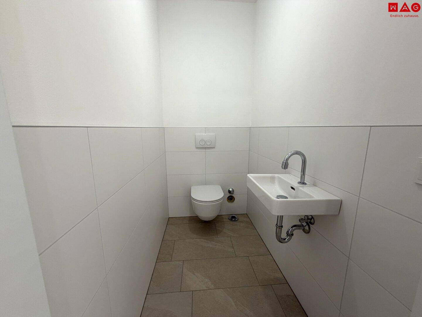 Helles Gäste-WC mit Wand-WC, kleinem Waschbecken und Fliesenboden.
