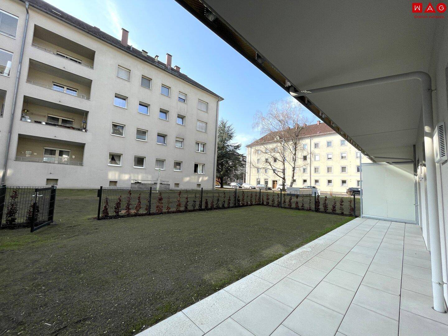 Geräumige Terrasse mit Fliesenboden und angrenzender Rasenfläche vor Wohngebäuden.
