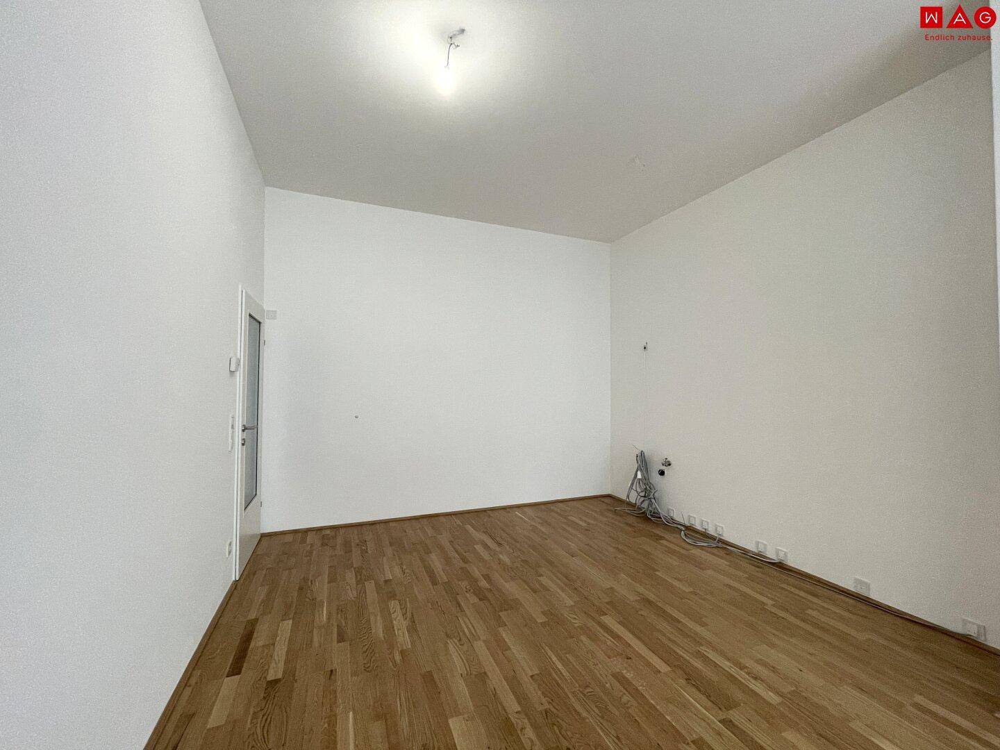 Leerer Raum mit Holzboden und Anschlüssen für eine zukünftige Küche.
