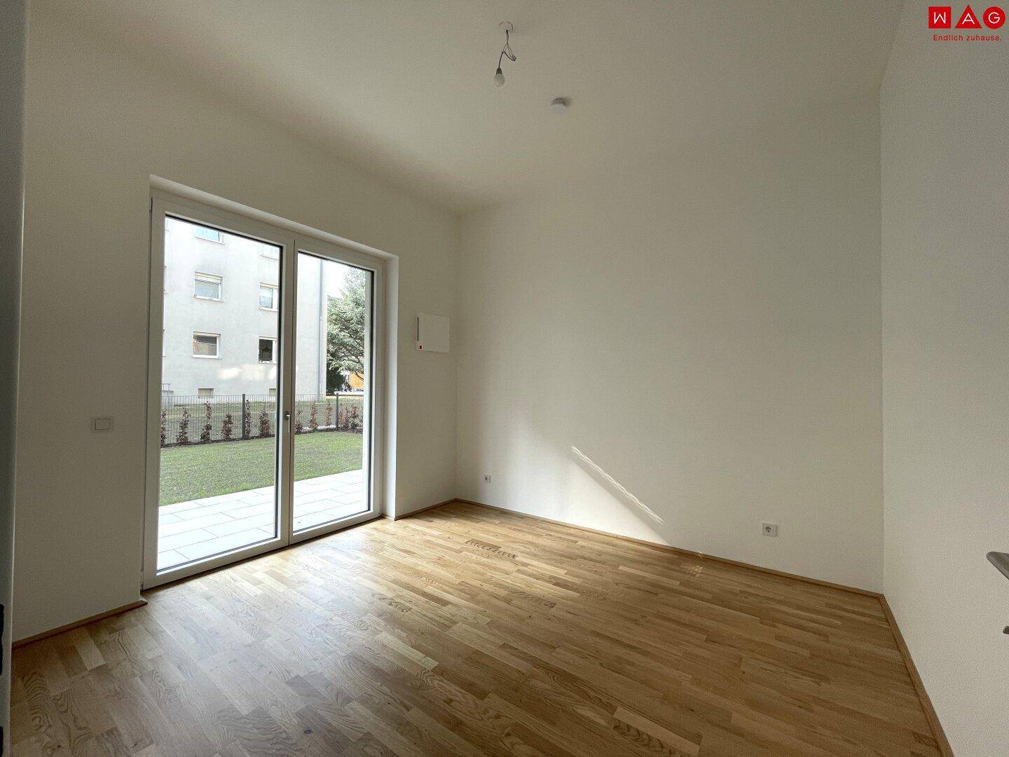 Helles Schlafzimmer mit Parkettboden und großem Fenster mit Blick auf die Grünfläche.