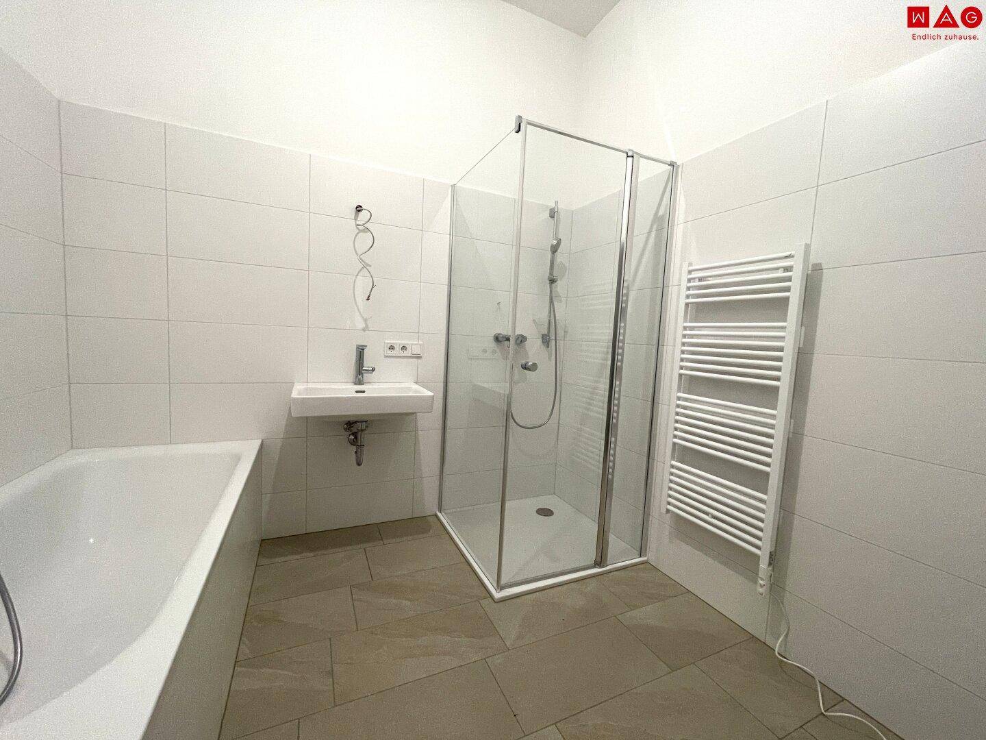 Helles Badezimmer mit Badewanne, Duschkabine und beheiztem Handtuchhalter.