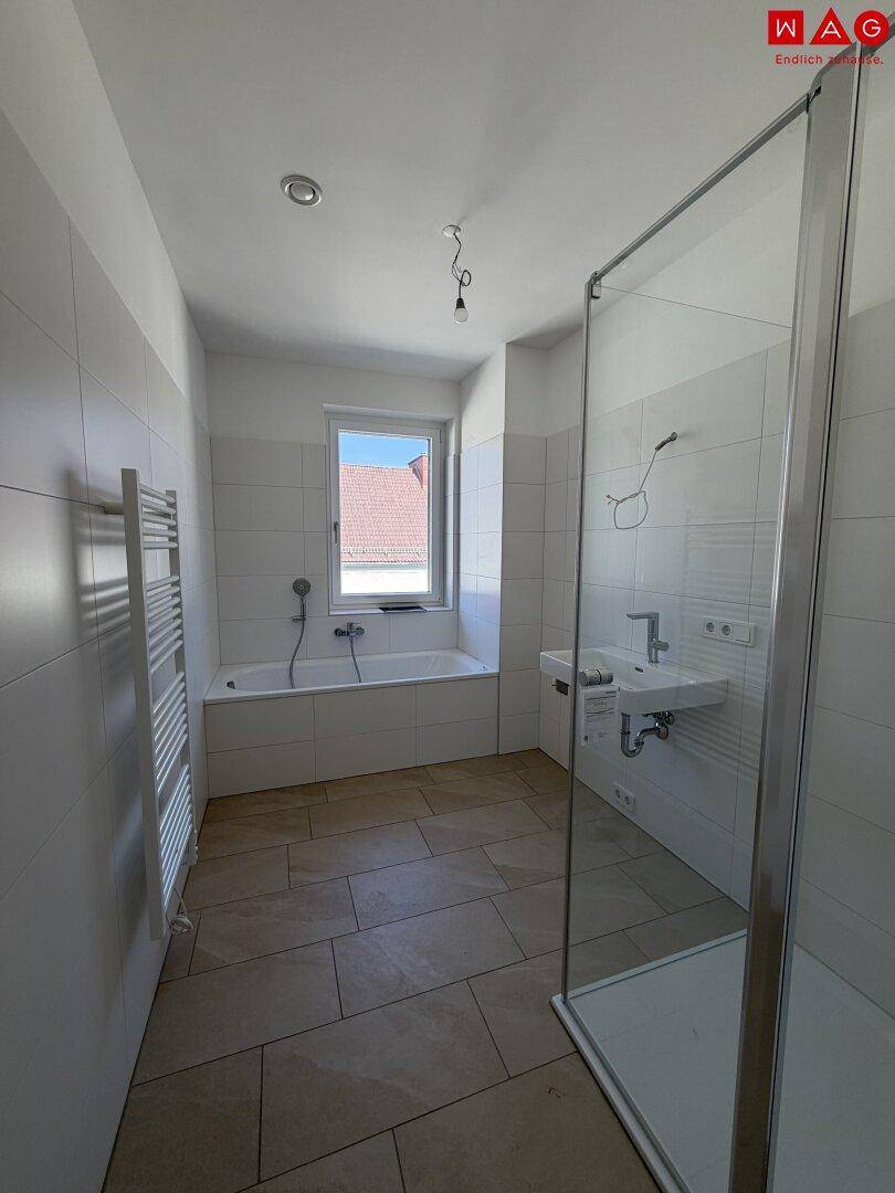 Leeres Badezimmer mit Badewanne, Duschbereich und Fenster, bereit für die Ausstattung.