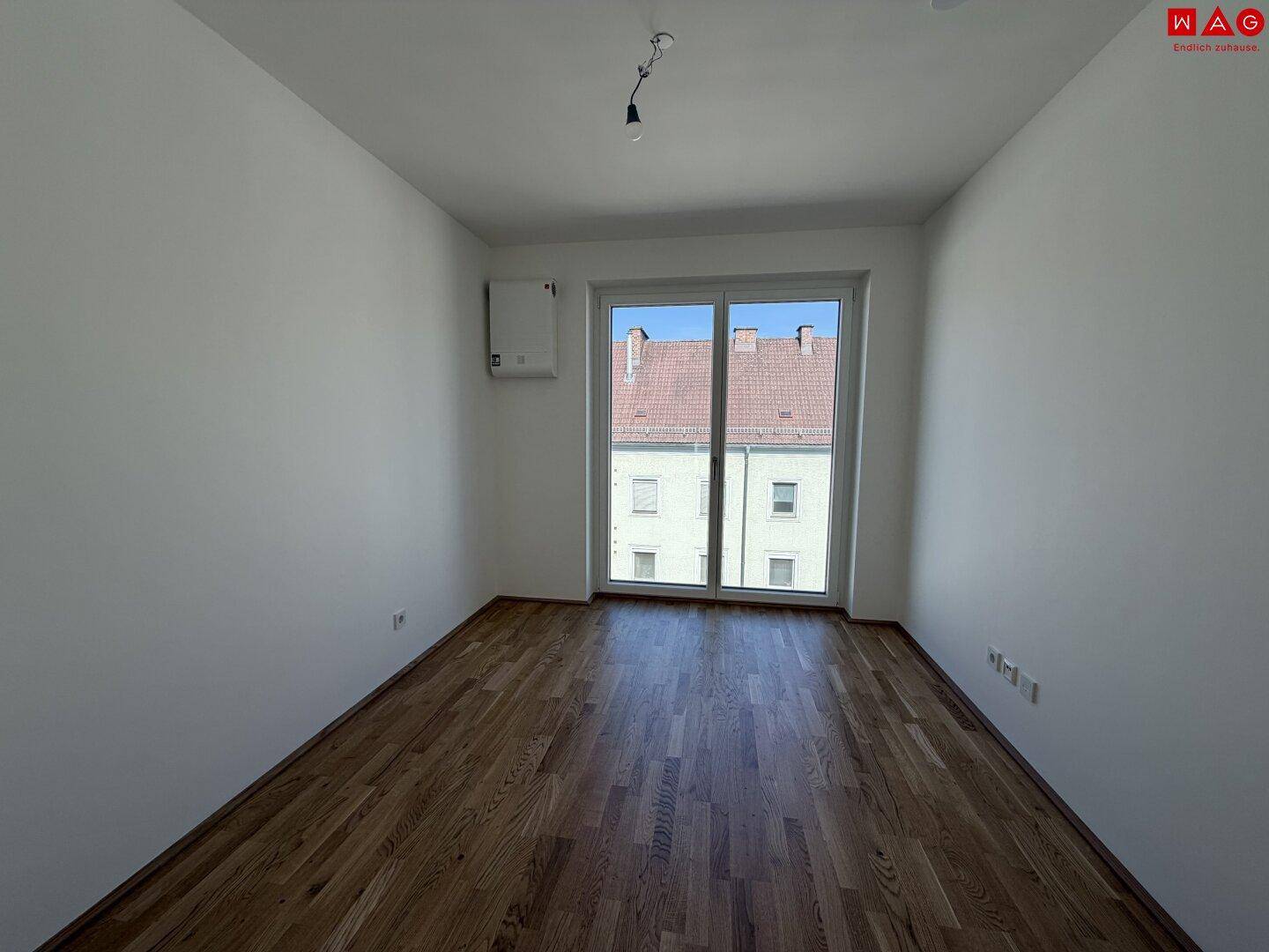 Leeres Zimmer mit Holzboden und großem Fenster, ideal als Kinder- oder Arbeitszimmer.