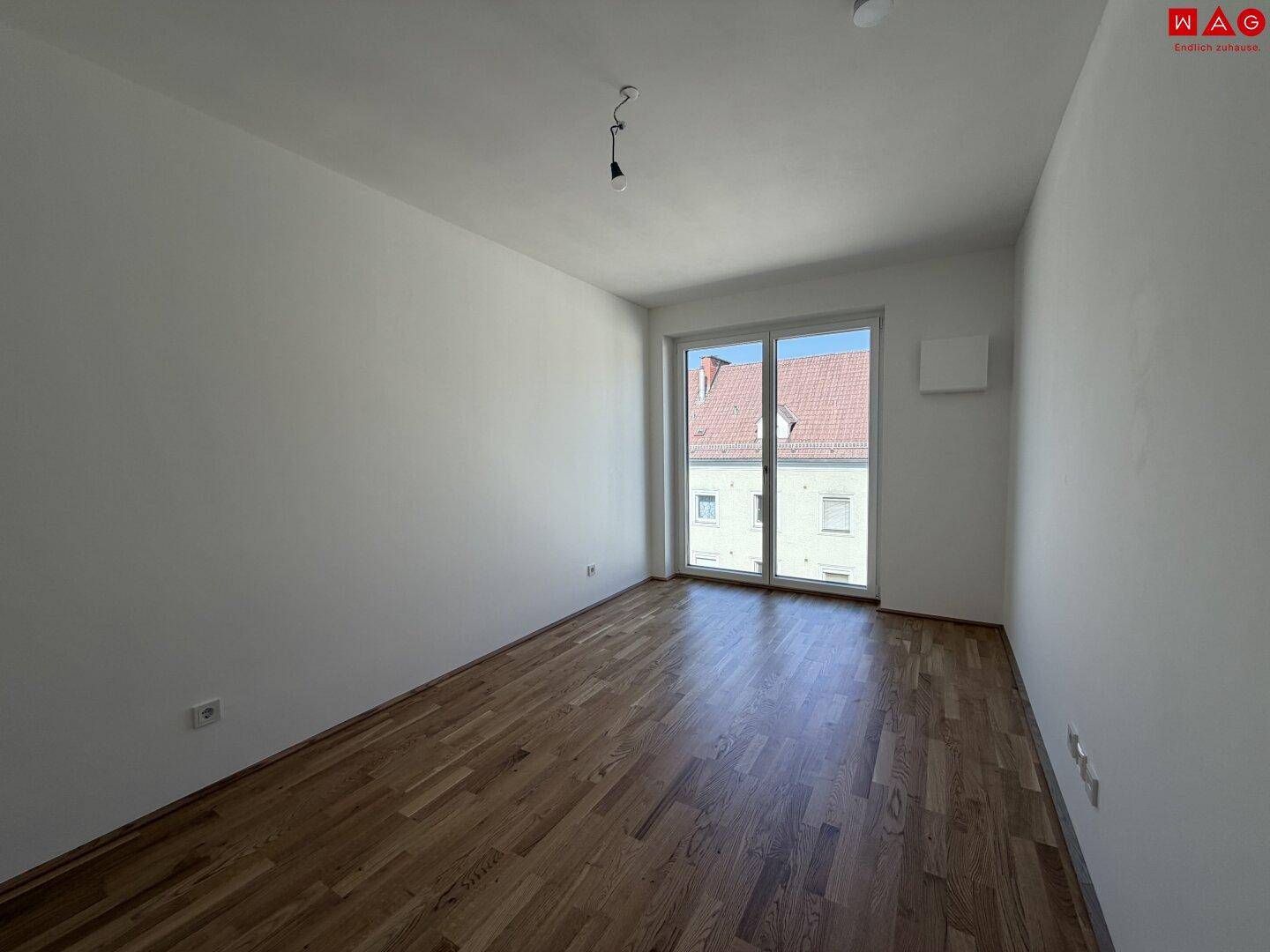 Leeres Schlafzimmer mit Holzboden und großem Fenster, bereit zur individuellen Gestaltung.