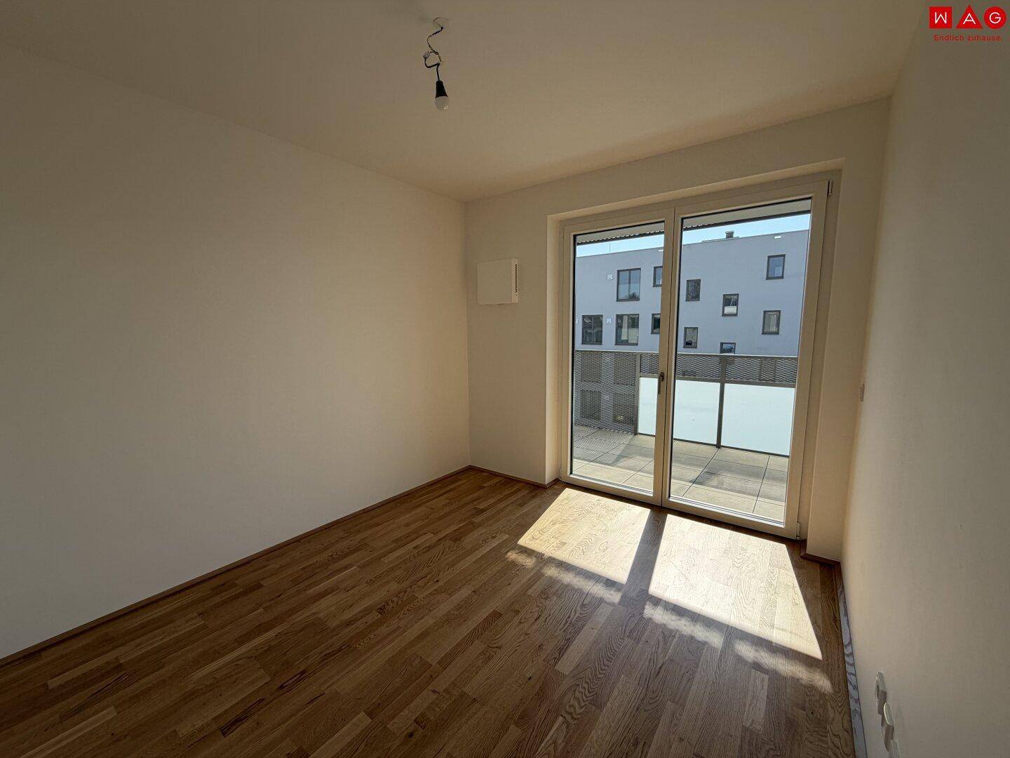 Leeres Zimmer mit Holzboden und Zugang zu einem Balkon, ideal als Arbeitszimmer.
