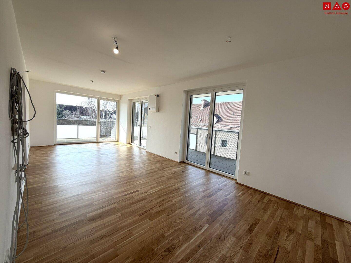 Lichtdurchfluteter Wohnbereich mit Holzboden und mehreren Zugängen zu Außenbereichen.