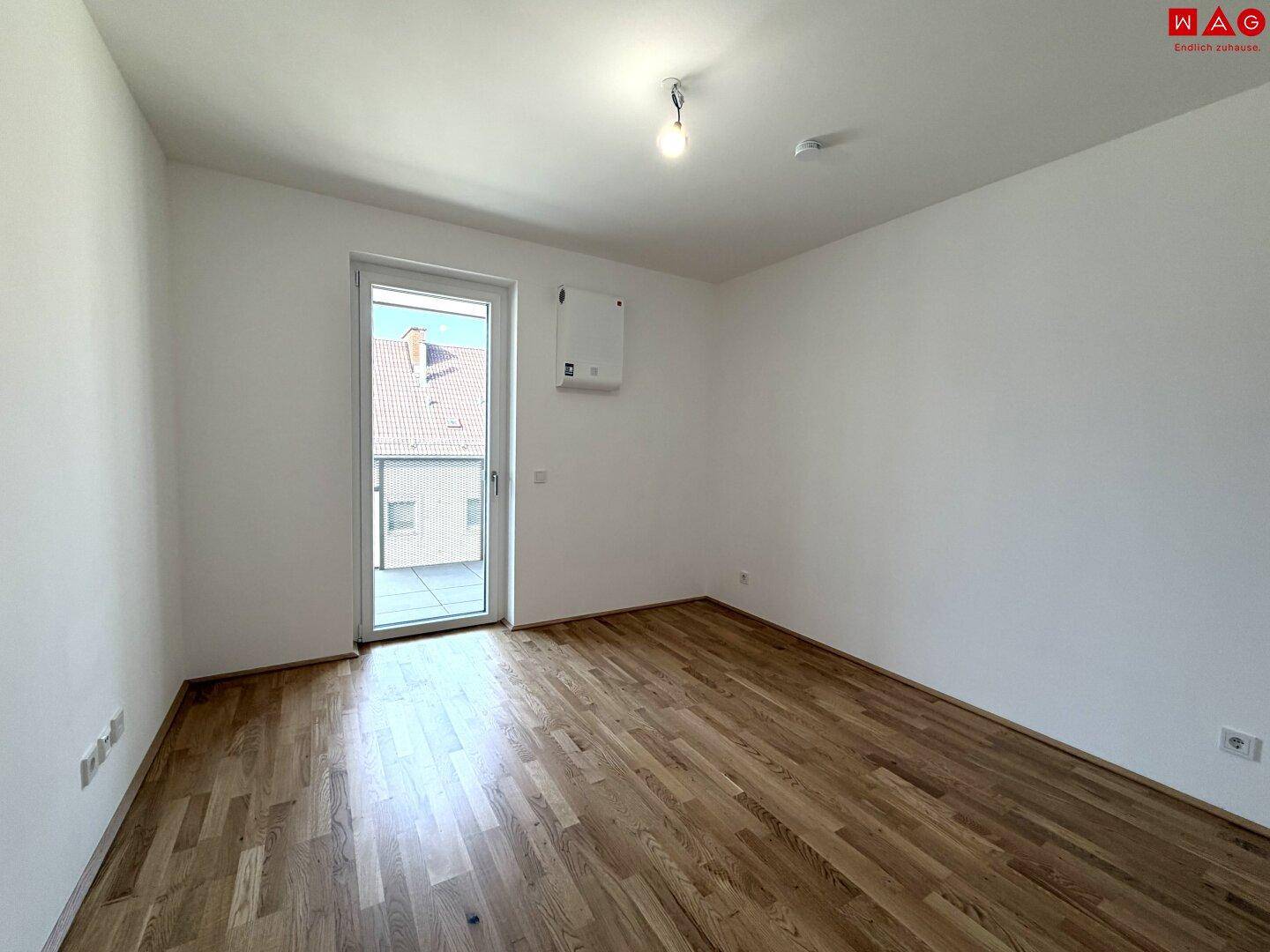 Leeres Schlafzimmer mit Holzboden und Balkontür, bereit zur individuellen Gestaltung.