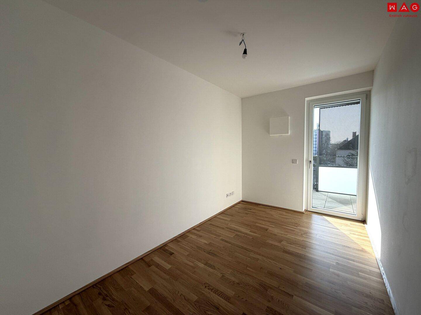 Leeres Zimmer mit Holzboden und Balkontür, ideal als Kinder- oder Gästezimmer.