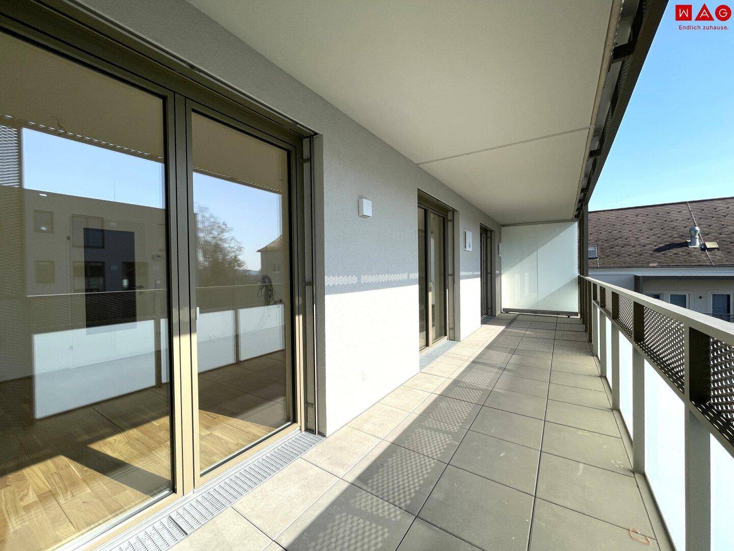 Breiter Balkon mit Fliesenboden und Blick auf die Umgebung, zugänglich von mehreren Räumen.