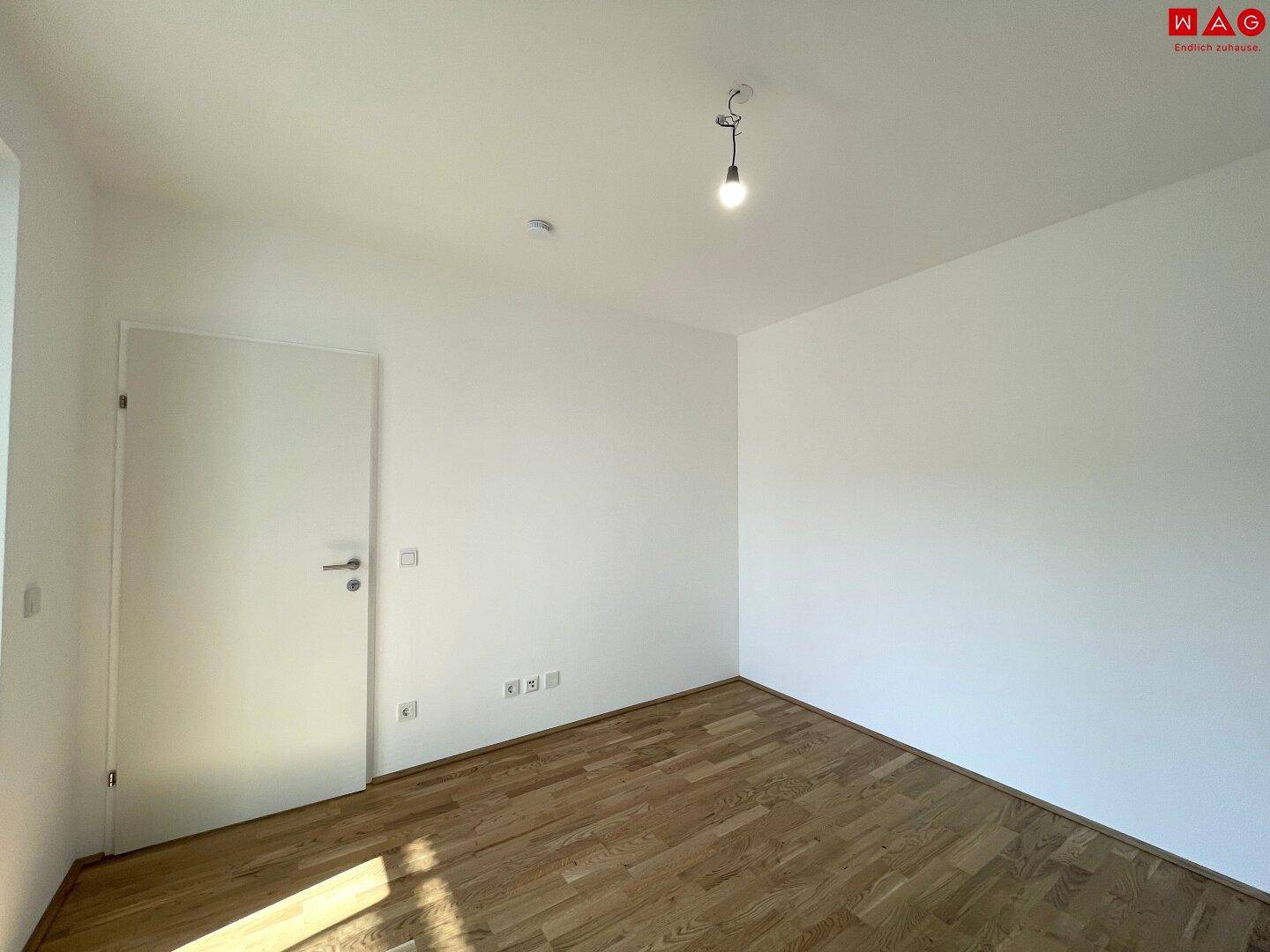 Leeres Zimmer mit Parkettboden und weiß gestrichenen Wänden, bereit zur individuellen Gestaltung.