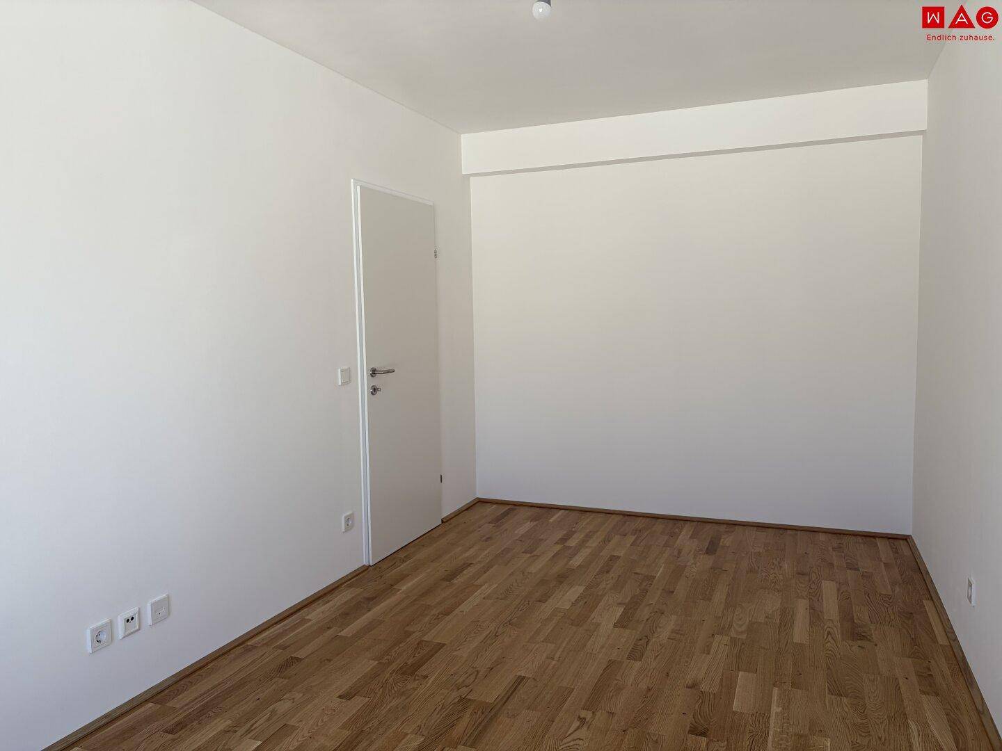 Leeres Zimmer mit Holzboden und weißen Wänden, ideal für flexible Nutzung.