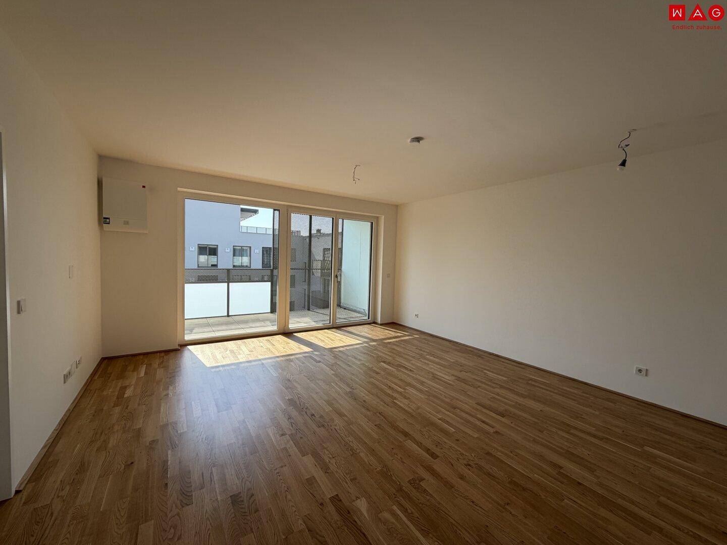 Geräumiger, leerer Wohn-Essbereich mit Holzboden und großen Schiebetüren zum Balkon.