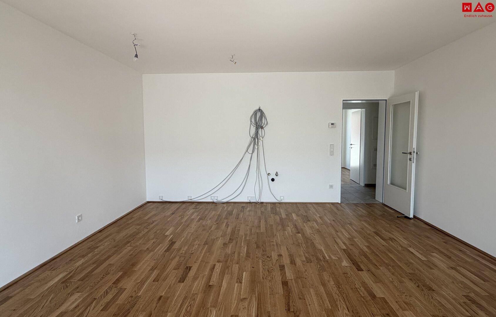 Leerer Raum mit Holzboden, weißen Wänden und vorbereiteten Elektroinstallationen.