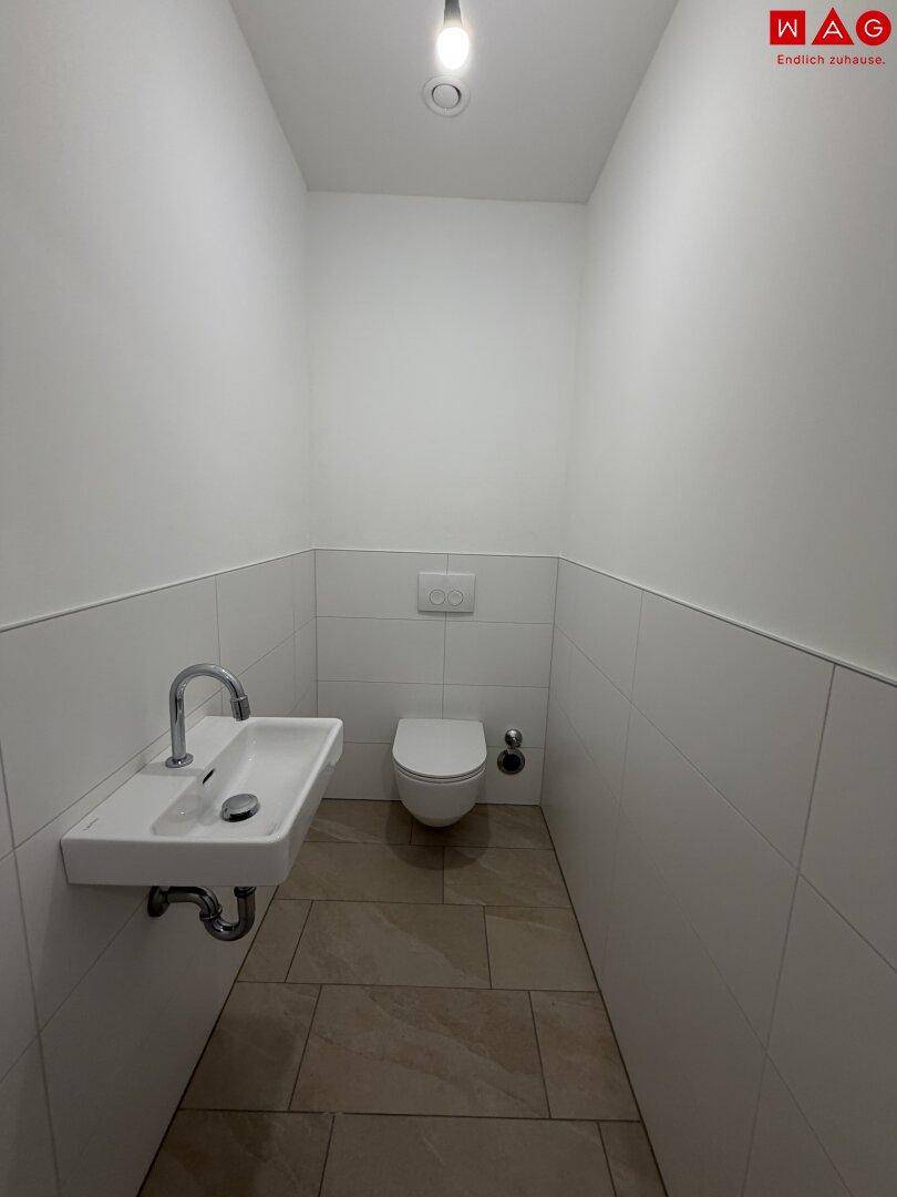 Leeres Gäste-WC mit wandhängendem WC und vorbereitetem Waschbeckenbereich.