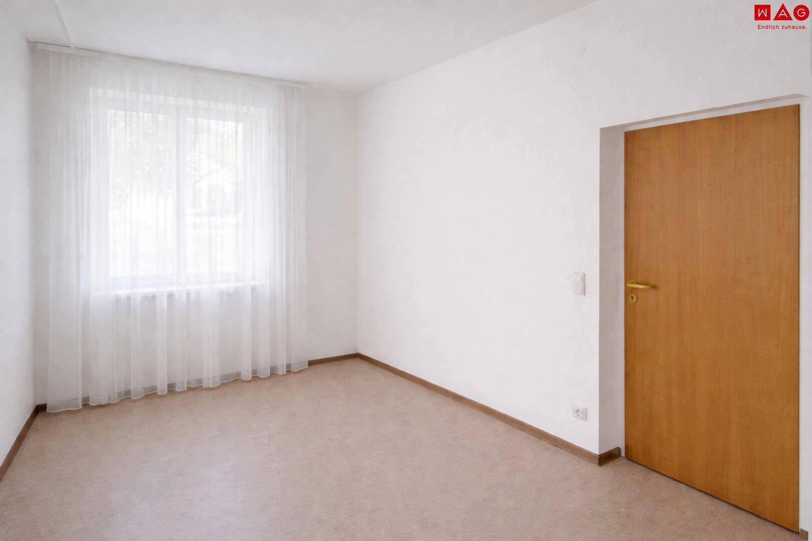 Heller, leerer Raum mit weiß gestrichenen Wänden, Vinylboden und einer Holztür.